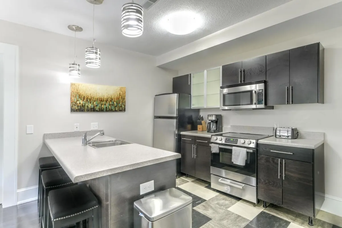 A bright, contemporary kitchen featuring a spacious island, stainless steel appliances, and eye-catching artwork on the wall. The room is well-lit and showcases both the modern renovations and inviting atmosphere, ideal for preparing meals or entertaining guests.
