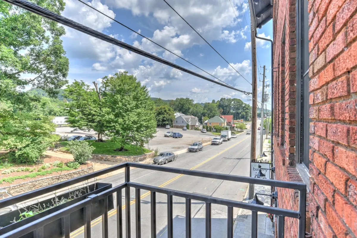 A broader street view framed by green trees and nearby buildings, with people strolling, sipping coffee on a balcony, and soaking up neighborhood life. The scene is both tranquil and lively, capturing the interplay of daily rhythms and community vibrancy.