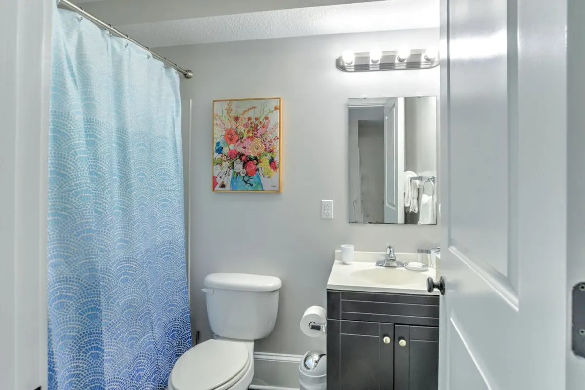 A bright and cheerful bathroom with a decorative shower curtain, a modern vanity featuring a sink and mirror, and colorful artwork on the wall. The room feels fresh, clean, and inviting, offering a peaceful space for personal care.